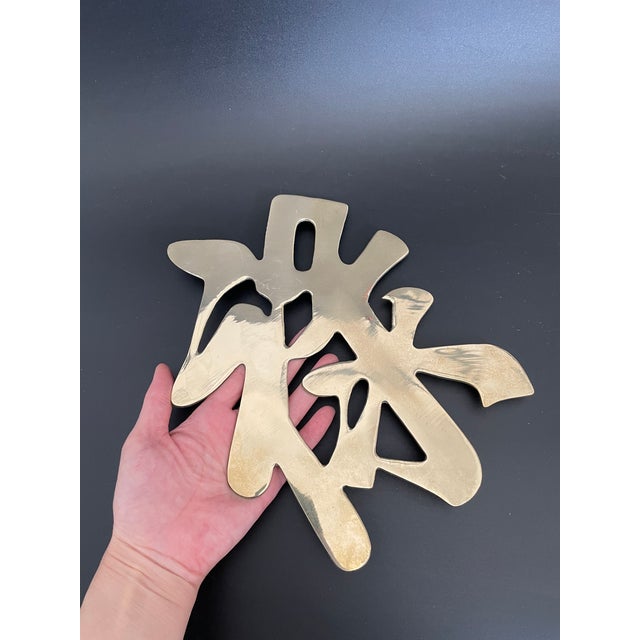 A vintage brass trivet in the form of the Chinese prosperity symbol. It is fitted with a hanging ring for wall display as...