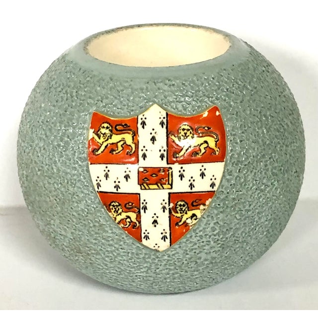 Made of Carlton Ware, this mid century Stoke on Trent match holder/striker is decorated with the crest of Cambridge...
