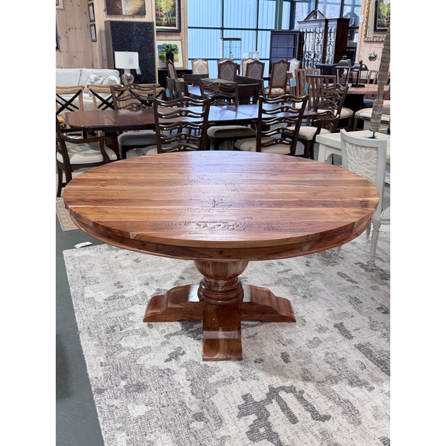 A richly toned solid wood dining table featuring a round plank-style top with beautifully varied grain and organic...