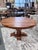 A richly toned solid wood dining table featuring a round plank-style top with beautifully varied grain and organic...