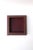 A square red burgundy textured leather jewelry catchall with gold tooling around top edge, by American luxury maker T....