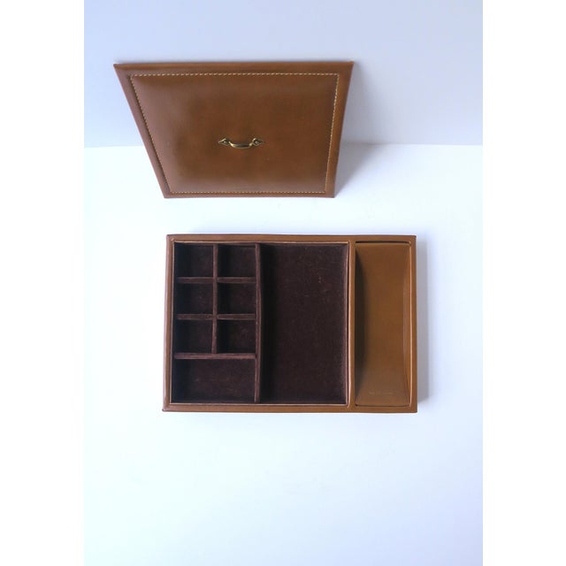 A leather jewelry box caddy with lid, circa mid-20th century. A tan camel/caramel colored leather jewelry box with a dark...