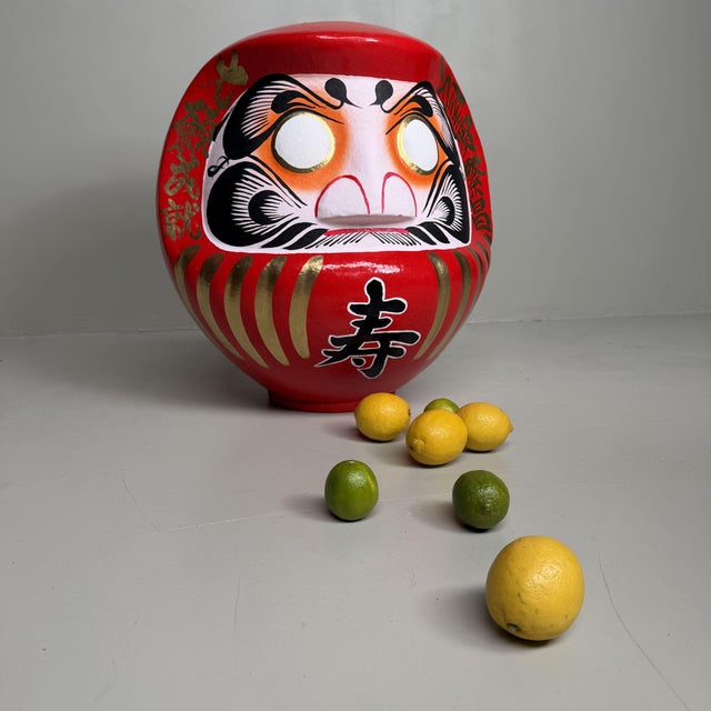 This impressive Daruma is a true statement piece: classic red with bold black-and-white facial features and gold accents....
