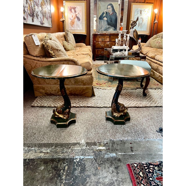 This pair of Italian-style accent tables stand on intricately carved pedestal bases featuring a mythological dolphin with...