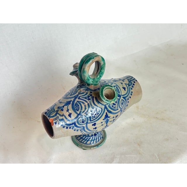 This glazed vessel terra cotta vessel has blue designs depicting curves, lines, and dots. The handle is celadon.