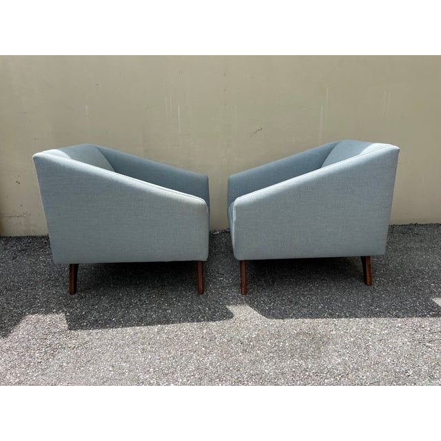Pair of mid century style lounge chairs. The chairs are done in a blue chenille. No pillows are included. The base is...