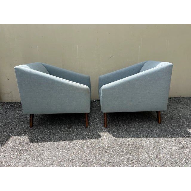 Pair of mid century style lounge chairs. The chairs are done in a blue chenille. No pillows are included. The base is...