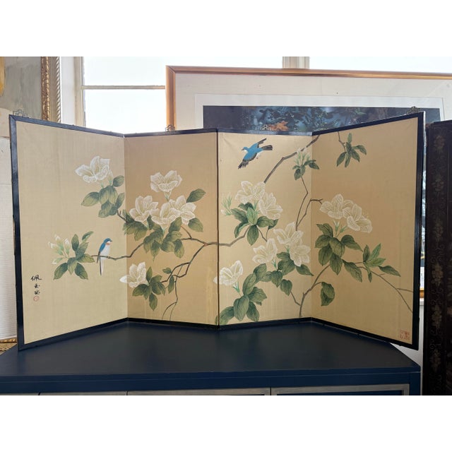 Hand painted four‑panel folding screen featuring magnolia branches and sky‑blue birds on a warm neutral ground, creating a...
