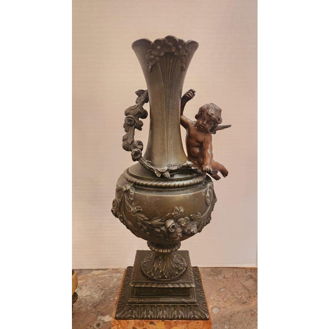 This listing features a pair of patinated bronze cherub ornamental vases in an Art Nouveau style of decoration. The vase...