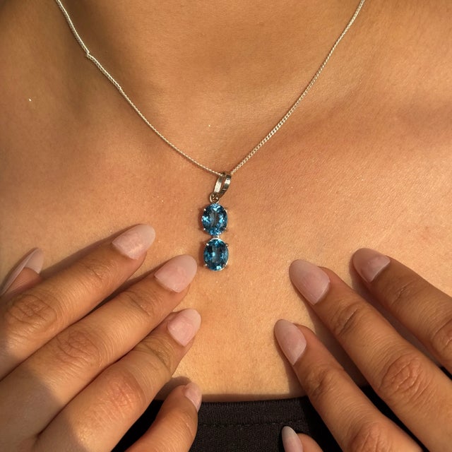 A refined expression of elegance, this 925 sterling silver pendant features two carefully selected oval Blue Topaz...