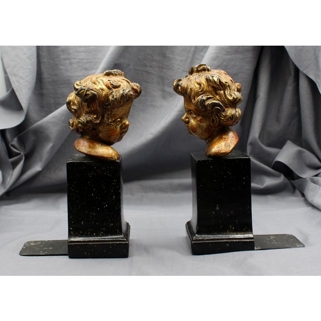 Mid-20th century pair of bookends, faux marble and plaster, likely Italian. Well modeled curly haired gilt plaster putti...