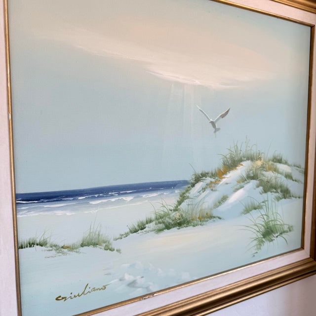 A signed vintage oil painting depicting a serene coastal landscape with white sand dunes, sea oats, rolling waves, and a...
