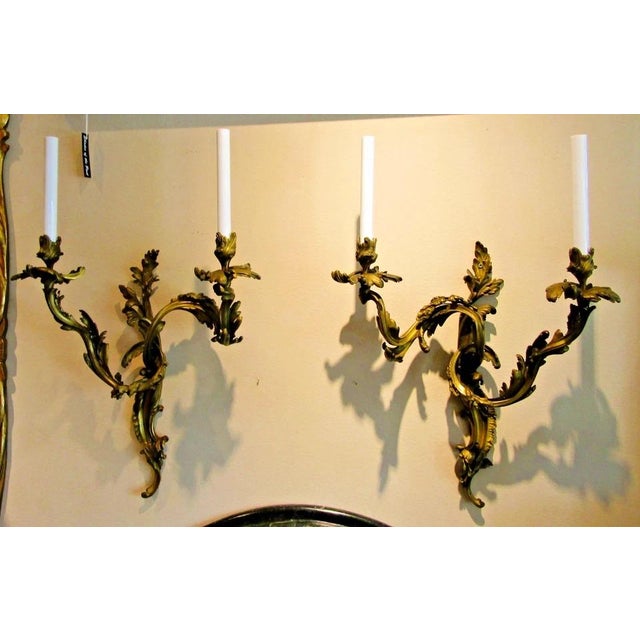 This antique pair of French 19th century Louis XV gilt bronze two light wall sconces exudes elegance and sophistication....