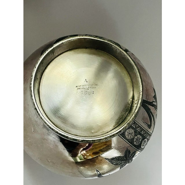 This silver-plate vessel features a charming garden scene. It is finished with an interlocking floral border and stylized...