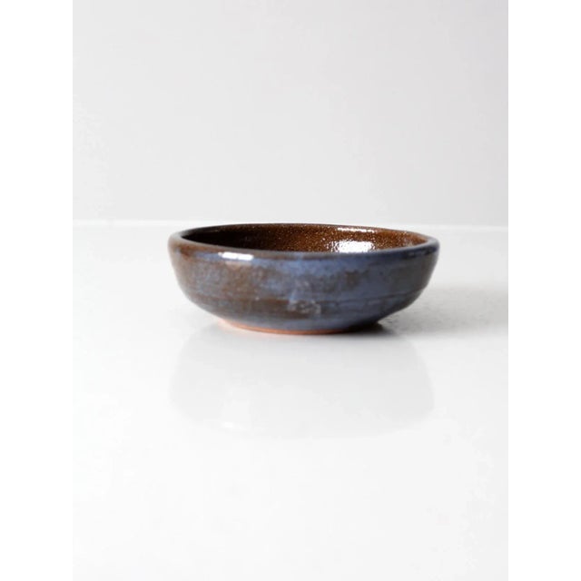 This is a vintage studio pottery bowl. Signed by the artist, the handmade shallow bowl features a blue and brown glaze...
