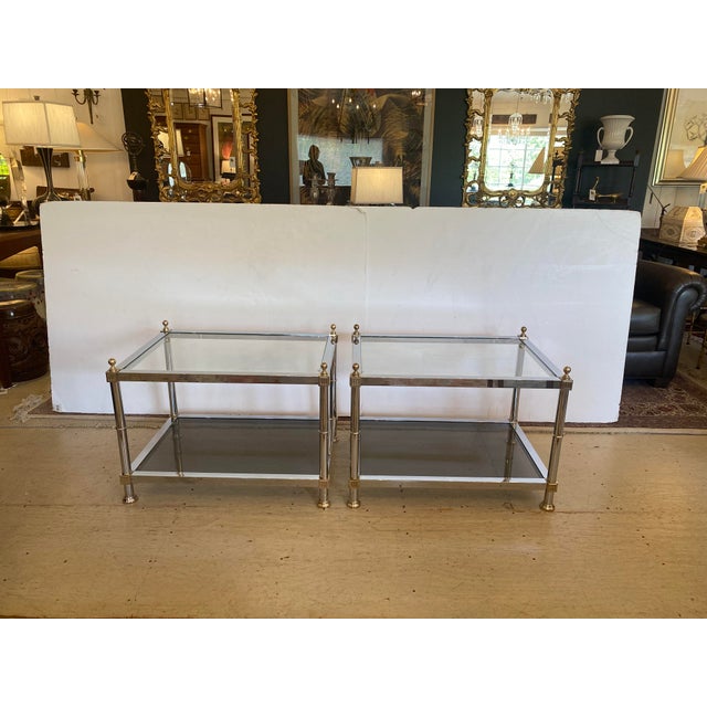 Sleek two tier end tables having polished chrome frames with handsome brass finials and neoclassical details....