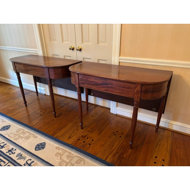 Pair of beautiful Mahogany Sheraton period demi-lune tables (circa 1820) featuring rear drop leaf, hand-turned legs, and...