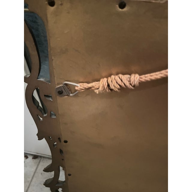 The mirror is a Baroque or Rococo-style ornate gold wall mirror. There is a hint of red beneath the shinny gold frame. It...