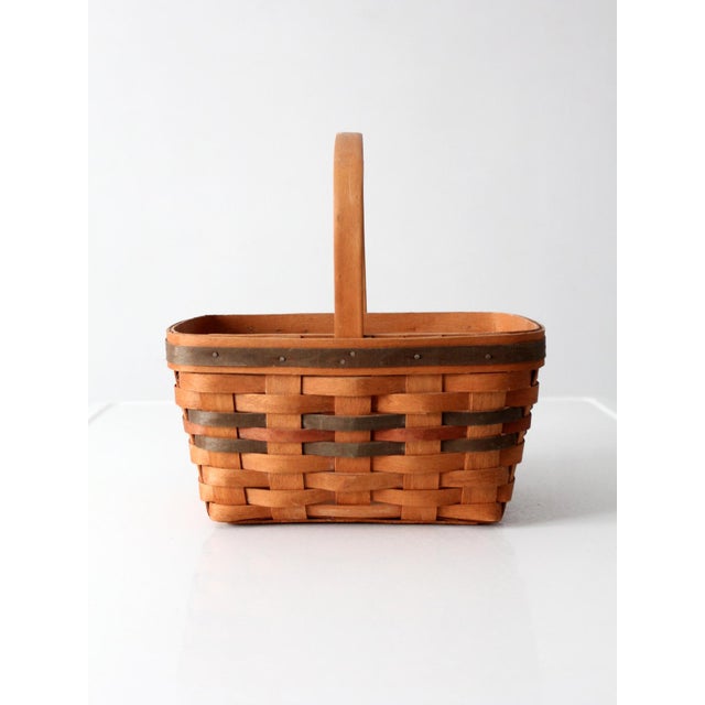 A vintage 1991 Longaberger handwoven market basket with warm honey-toned weaving accented by red and green bands along the...