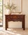 A Chinese altar-style table in warm reddish wood, with a plank top, two drawers and a deeply carved apron. The apron is...