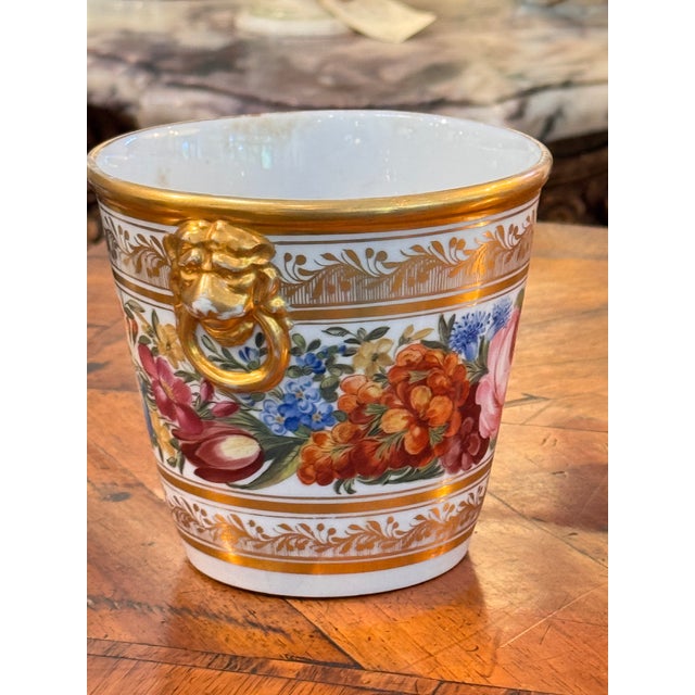A three-piece porcelain cachepot set, each richly hand-painted with colorful floral garlands and detailed with gilt...