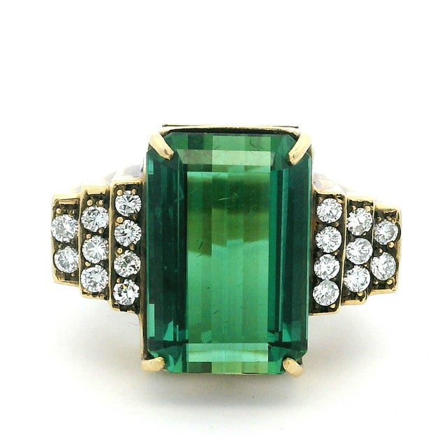 A dramatic 1970s cocktail ring centered by a monumental emerald-cut green tourmaline weighing approximately 10 carats. The...