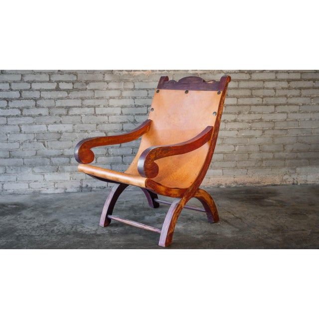 Vintage Clara Porset Butaque style armchair. Low slung leather sling seat and curule-style base. Elegant curvature and...