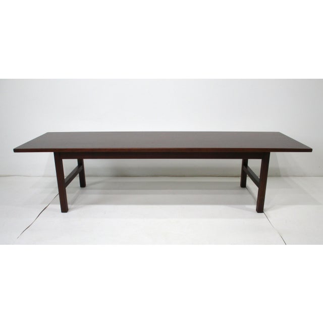 A dark walnut coffee table with a pleasing simple aesthetic in the manner of Danish modern design. Manufactured in the...