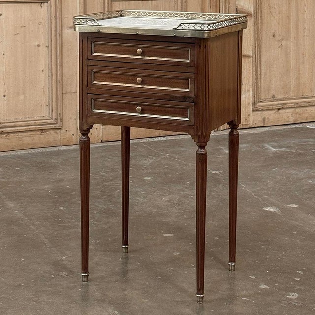 Elegant mid-century French Louis XVI bedside table crafted in richly toned mahogany and crowned with luminous Carrara...