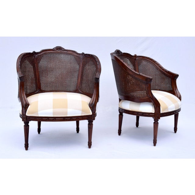A pair of French Louis XVI style double caned Bergere chairs of classic European styling with carved wood frames, tight...