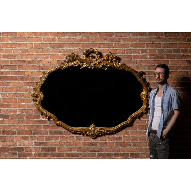 An ornate Rococo Revival wall mirror featuring a gilded wood frame with flowing foliate and floral motifs. The crest is...