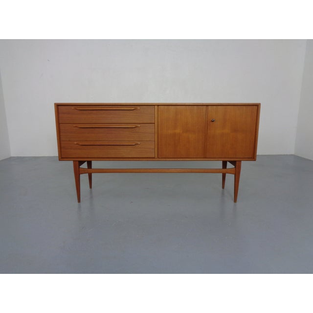 Small teak sideboard from the 1960s. Design by Heinrich Riestenpatt. Two doors with a shelf behind them. Three drawers on...