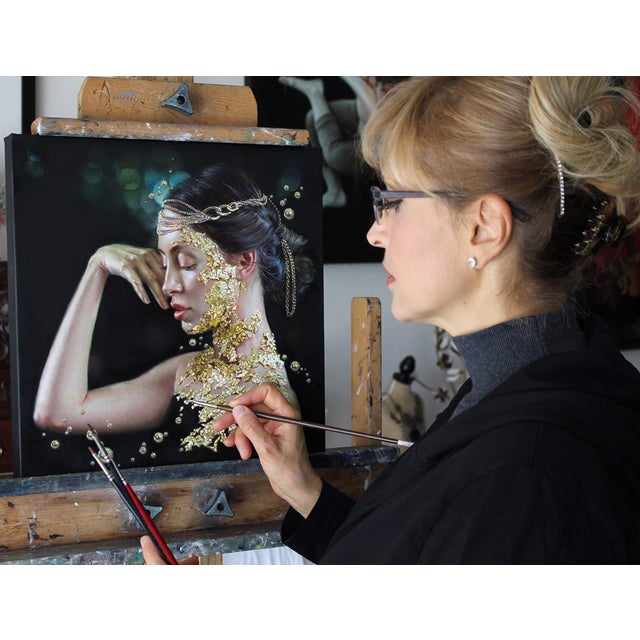 This artwork presents a serene profile of a woman adorned with shimmering gold leaf, which appears to cascade from her...