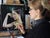 This artwork presents a serene profile of a woman adorned with shimmering gold leaf, which appears to cascade from her...