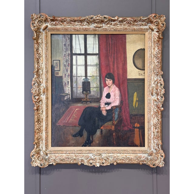An early 20th century oil on board depicting a young woman seated in her drawing room, rendered with warm interior tones...