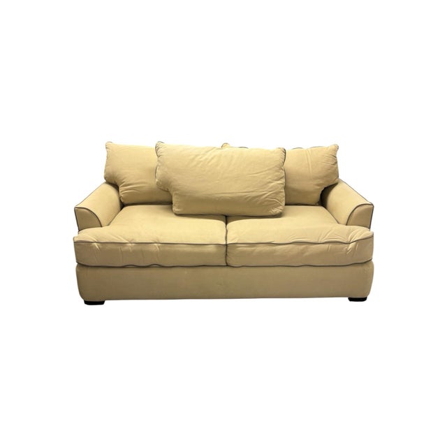 Unmarked tan sleeper sofa with a woven fabric texture and dark navy piping along the edges. It pulls out to a full-size...