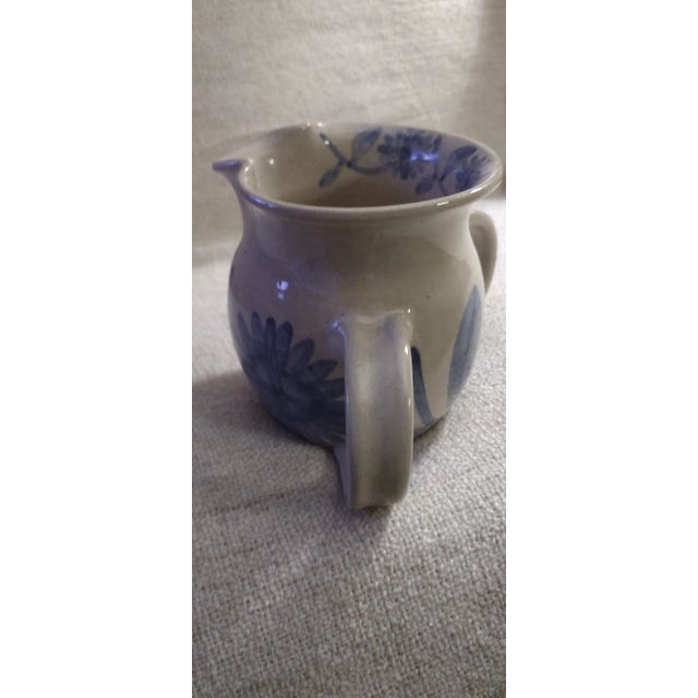 A Sonny Flechard "PLEASE PASS THE GRAVY PITCHER" design, 1990's. A 2 handle pitcher with a glazed blue floral design. With...