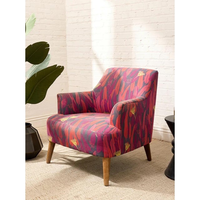 A bold modern accent chair upholstered in a vibrant botanical-patterned fabric featuring expressive layers of red,...