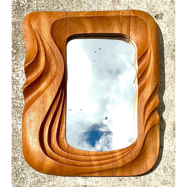 This exceptional vintage mirror is a masterclass in organic modernism, featuring a hand-carved frame that flows with...
