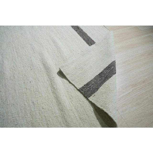 This hand woven wool rug features a primary color palette of ivory, beige, cream, and white. Crafted in India, the kilim...