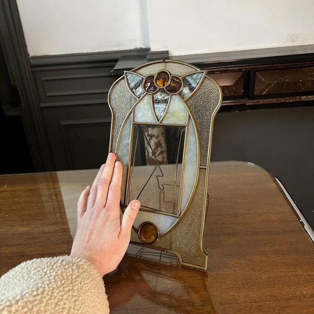 Stand-mounted brass photo holder, diamond-cut glass cabochons & stained glass. Both Art Nouveau and Art Deco in style, it...