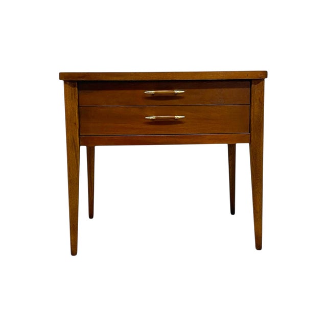 This vintage Mid-Century Modern end table features clean lines, tapered legs, and a warm wood finish characteristic of...