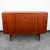 Danish modern high-board credenza in teak with a center rosewood bar. This cabinet features 4 sliding doors, 3 drawers, an...