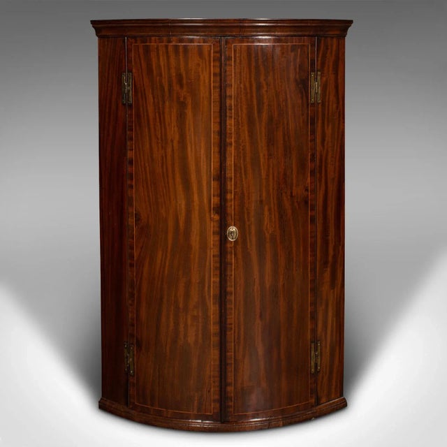This is an antique corner cabinet. An English, mahogany and oak bow front wall cupboard, dating to the Georgian period,...