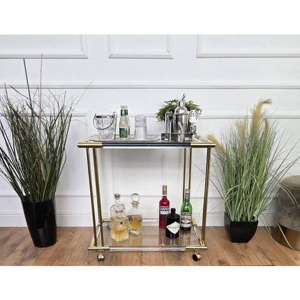 Beautiful and stylish 1960s Hollywood Regency Italian two-tier brass and plexiglass bar cart. A great piece that perfectly...