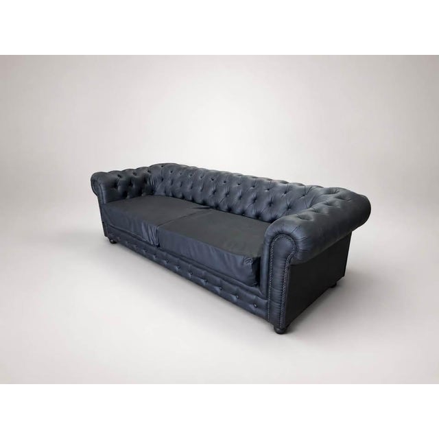 A dark charcoal Chesterfield-style sofa with classic deep tufting, rolled arms, nailhead trim, and a strong sculptural...