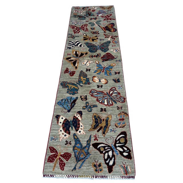 A pictorial runner filled with butterflies, hand-knotted in northern Afghanistan from hand-spun Ghazni wool. On a natural...