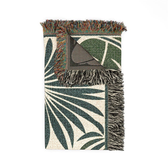 This tropical palm leaf woven throw blanket features oversized teal-green and olive foliage on warm cream with a green...
