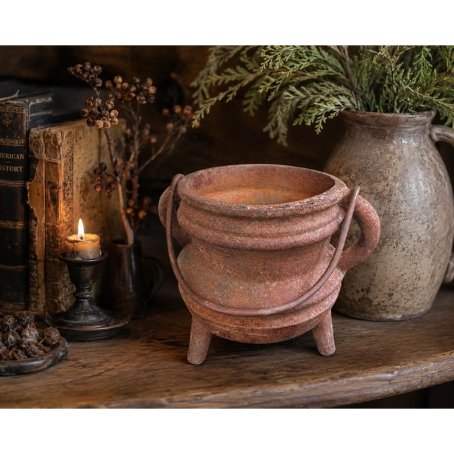 A beautifully aged antique primitive cast iron cauldron featuring three sturdy legs and an old swing bail handle, possibly...