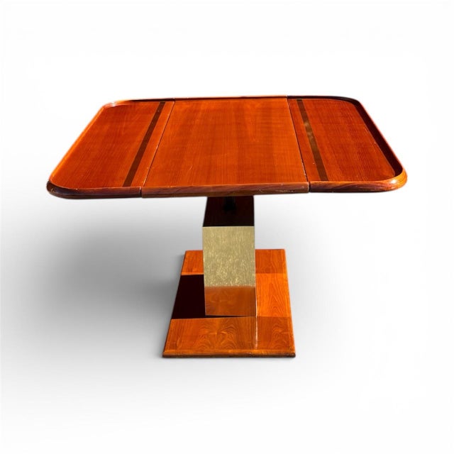 Striking Mid-Century Modern drop-leaf dining table featuring a sculptural central pedestal base clad in brushed brass and...